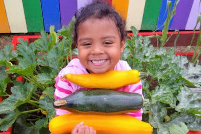 little girl smiling carrying vegetables