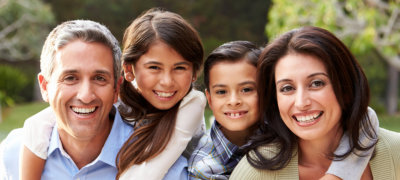 Portrait Of Hispanic Family In Countryside Giving Children Piggybacks Smiling At Camera